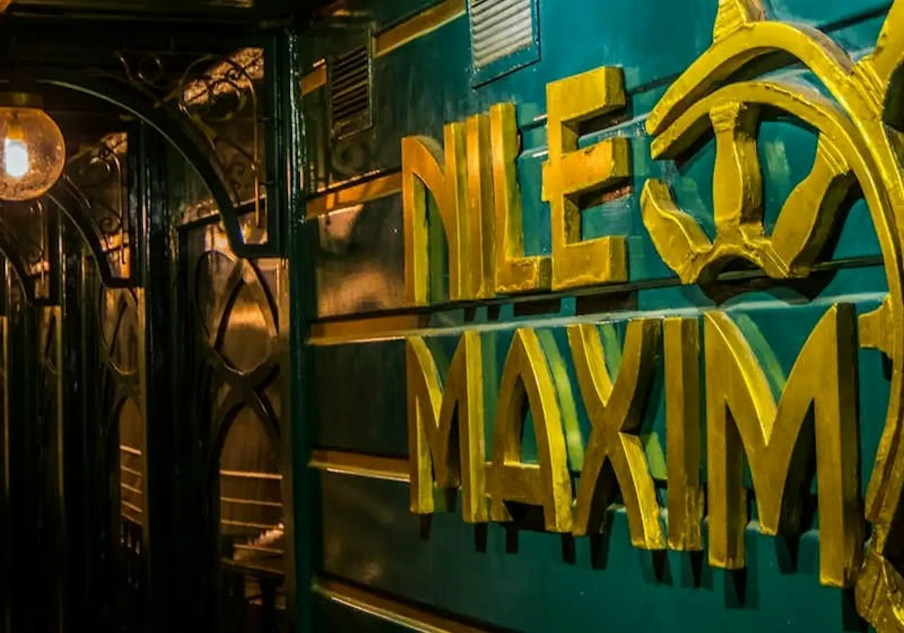 A teal wall with yellow decorative text reading "Nile Maxim," with ornate black ironwork and warm lighting nearby.