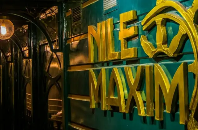A teal wall with yellow decorative text reading "Nile Maxim," with ornate black ironwork and warm lighting nearby.