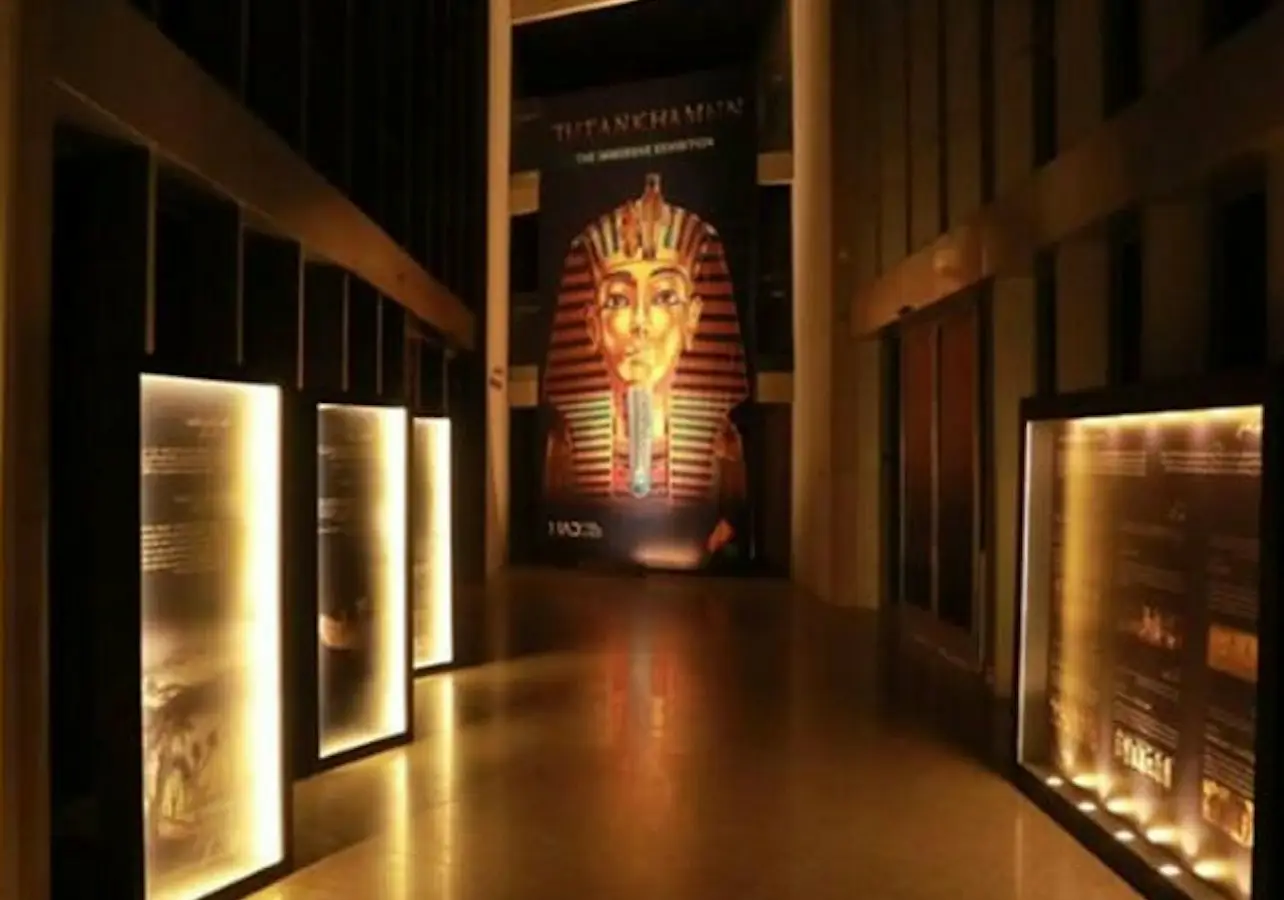 Dimly lit hallway with illuminated display panels and a large image of Tutankhamun's mask at the end.