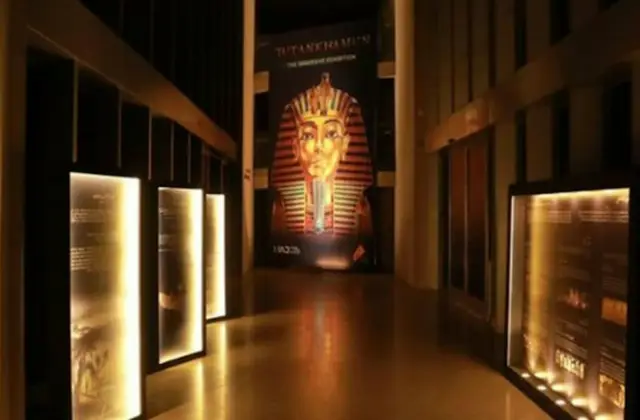 Dimly lit hallway with illuminated display panels and a large image of Tutankhamun's mask at the end.