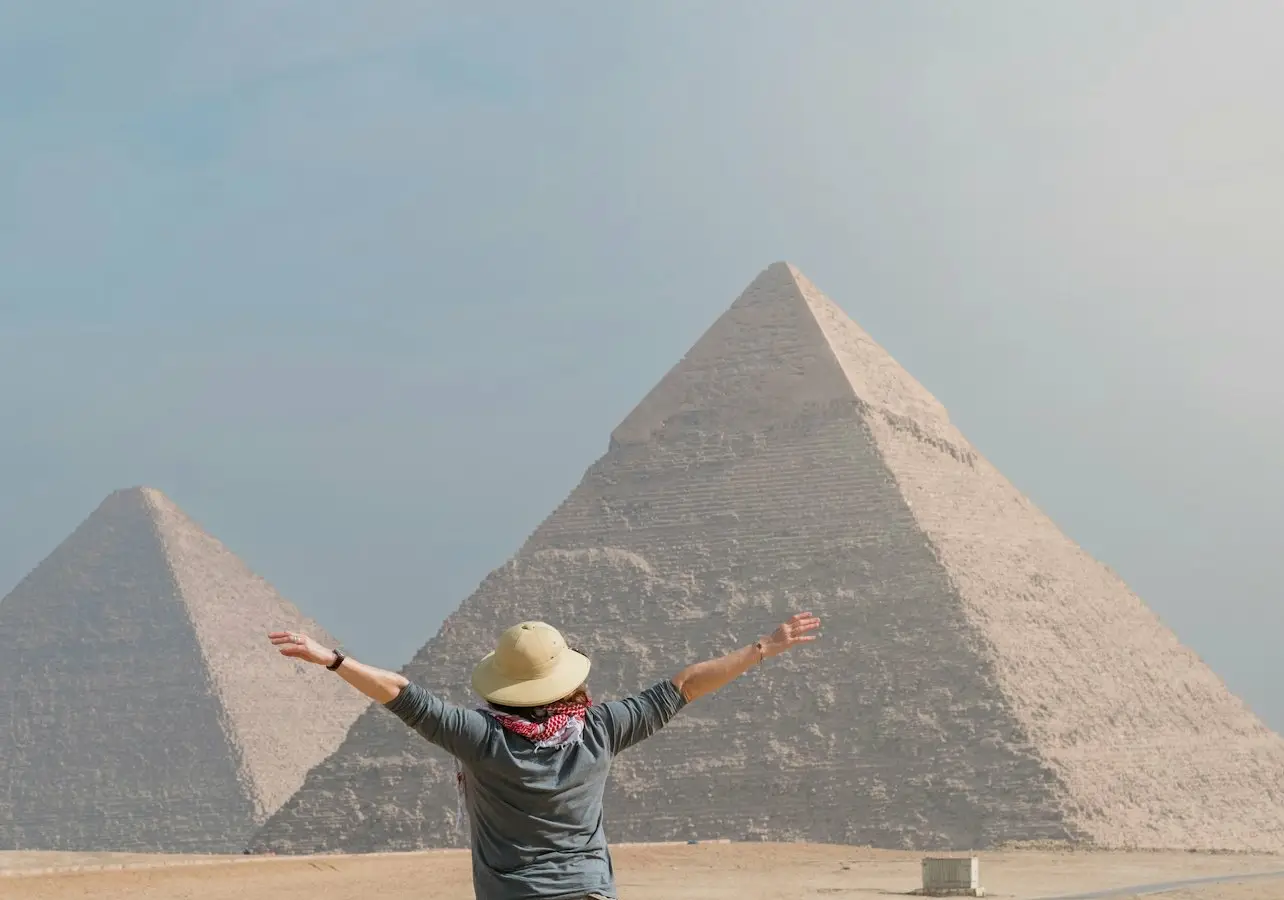 Person with outstretched arms facing the pyramids of Giza on a clear day.