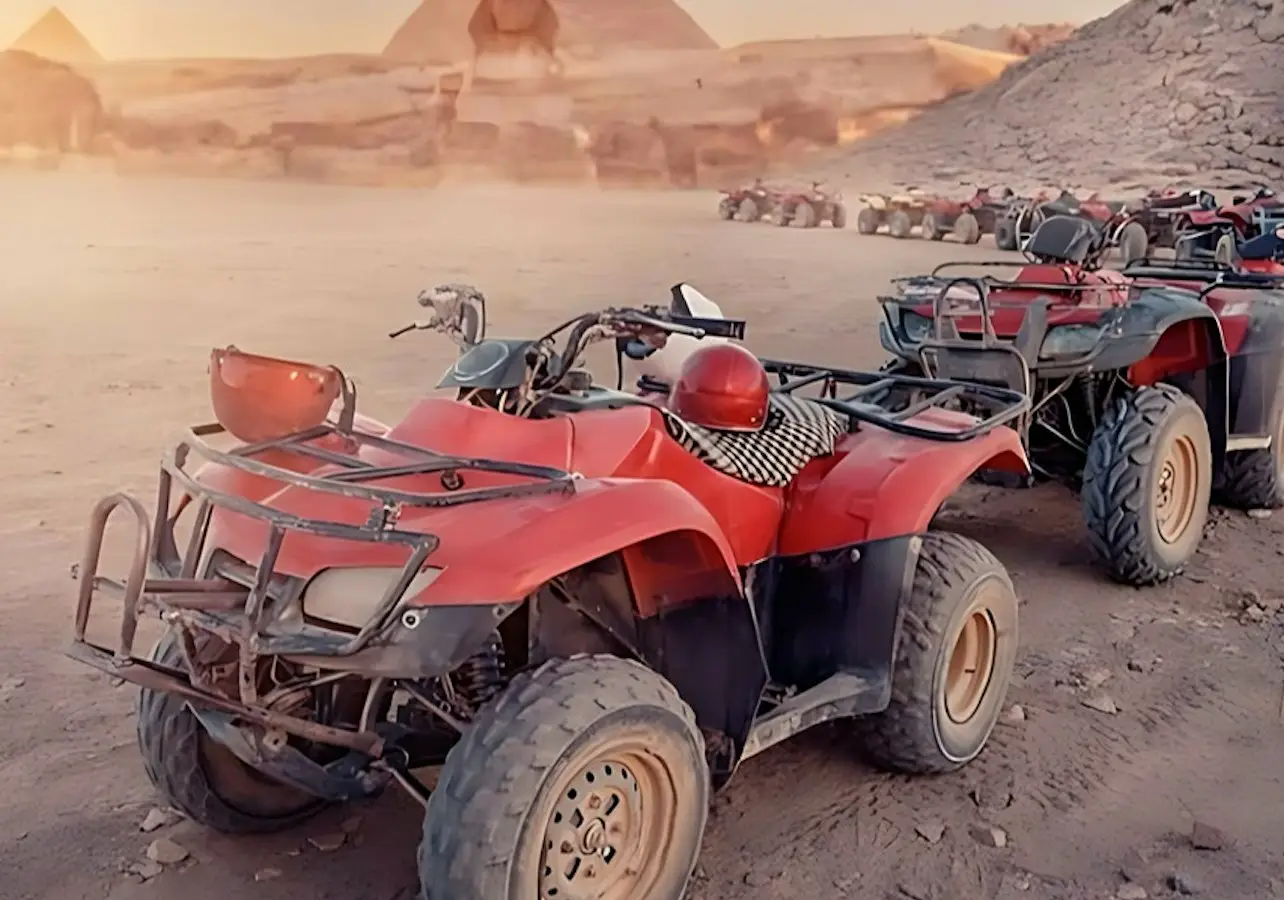 Several red all-terrain vehicles parked on a desert landscape with pyramids and rocky surroundings in the background.