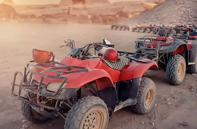 Several red all-terrain vehicles parked on a desert landscape with pyramids and rocky surroundings in the background.