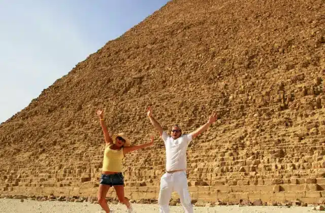 Two people jumping in front of the Great Pyramid of Giza, clear sky in the background.