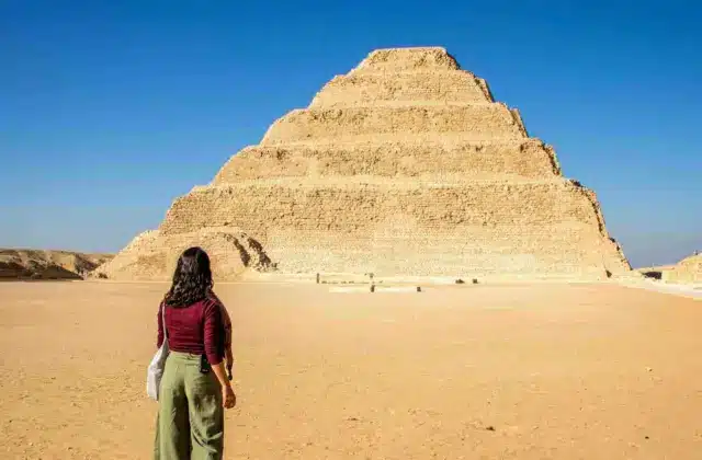 A person walking towards the Step Pyramid of Djoser under a clear blue sky in a desert setting.